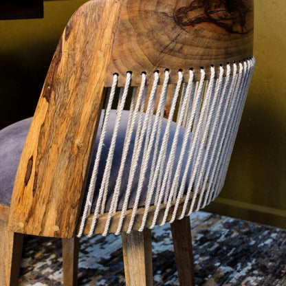 A close-up of a rustic wooden chair back with a thick natural wood slab, white rope wrapped vertically, and a blue-gray upholstered seat cushion.