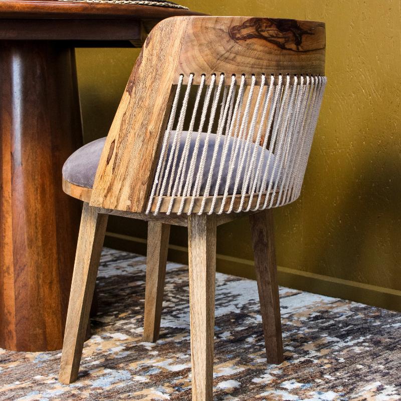 A rustic wooden dining chair with a thick natural wood backrest, white rope string details, and a gray upholstered seat cushion, shown in a dining room setting next to a wooden table.
