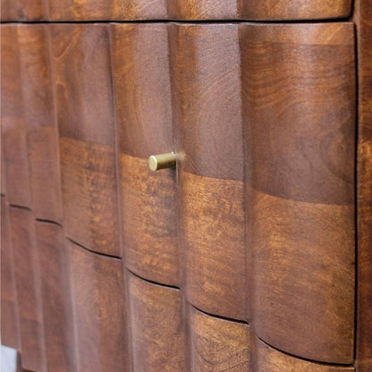 Close-up of a wooden cabinet or dresser with a wavy, vertically grooved front and a small round brass pull handle.