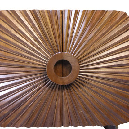 A close-up of a wooden cabinet or door featuring a radial sunburst design with radiating wood-grain panels and a circular center medallion.