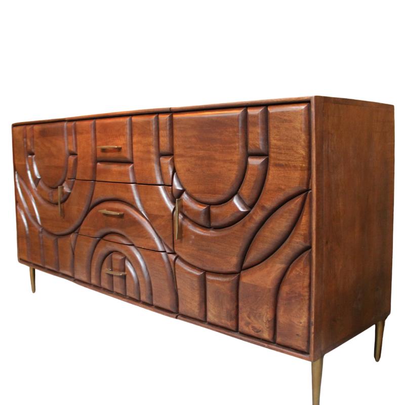 A mid-century modern wooden credenza with sculptural, curved carved drawer fronts and brass legs, set against a mustard yellow wall.
