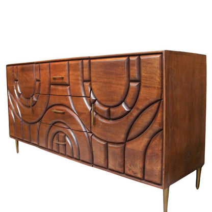 A mid-century modern wooden credenza with sculptural, curved carved drawer fronts and brass legs, set against a mustard yellow wall.