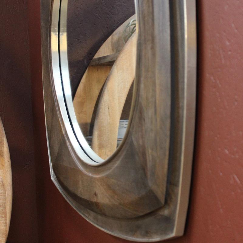 A close-up of a decorative wall mirror with a thick, rustic metallic frame mounted on a textured reddish-brown wall.