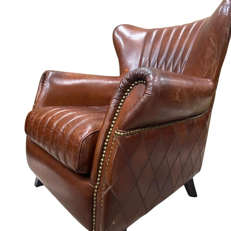A brown leather armchair with quilted stitching, tufted backrest, rolled arms with brass nailhead trim, and dark legs, shown on a plain white background.
