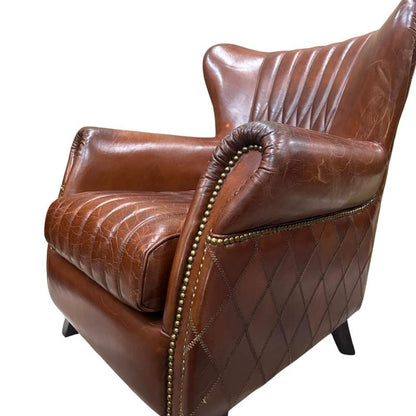 A brown leather armchair with quilted stitching, tufted backrest, rolled arms with brass nailhead trim, and dark legs, shown on a plain white background.