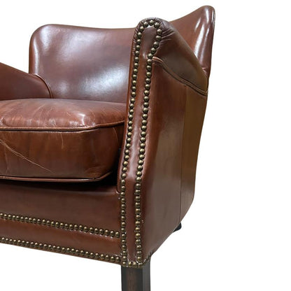 Close-up of a brown leather armchair showing the backrest, cushion, and rolled arm with brass nailhead trim against a white background.