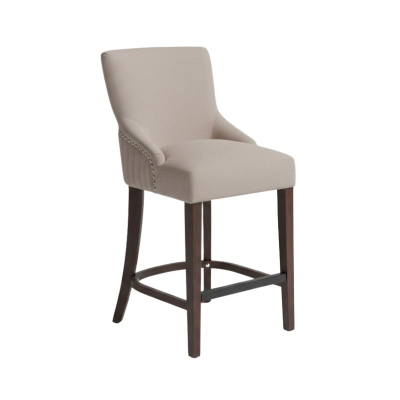 An upholstered bar stool with a light beige fabric seat and backrest, dark brown wooden legs, and silver nailhead trim on the armrest, shown against a plain white background.