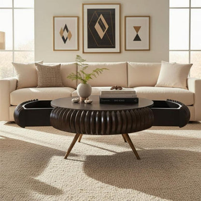 A modern round coffee table with a dark ribbed circular base and angled wooden legs, styled in a bright living room in front of a cream sofa.