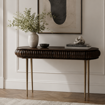 A dark brown ribbed console table with slim gold-toned legs, styled in a home interior with a ceramic vase, books, and a small bowl against a white paneled wall.
