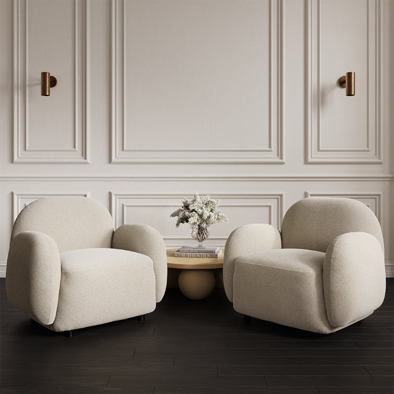 Two beige armchairs in a room with a decorative wall and small table.
