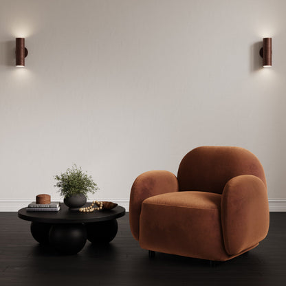 Brown armchair in a modern living room with a black coffee table and wall lights.