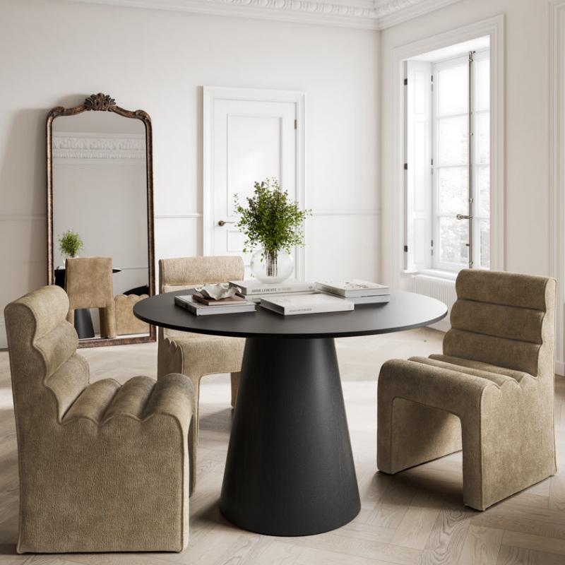 A modern dining set in a bright, classic room with white walls and ornate molding. The set includes a round black table on a tapered base, flanked by two beige upholstered armchairs and a matching armchair at the back, with a tall decorative mirror on the left.