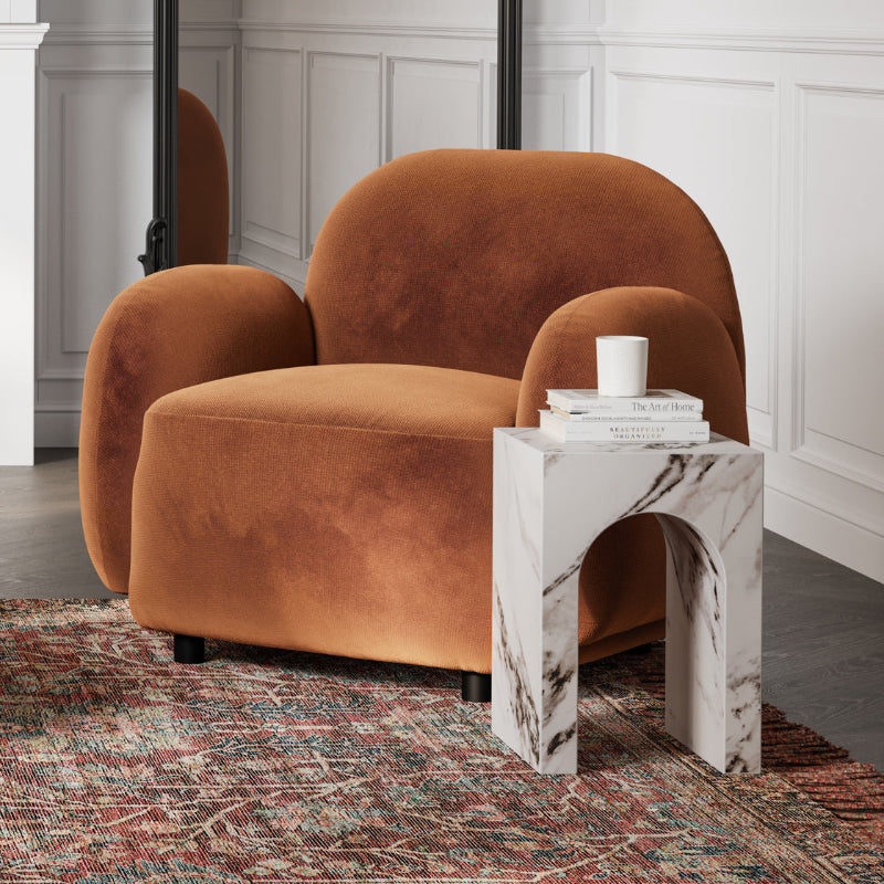 Brown armchair next to a marble side table with a white cup and books on a patterned rug.