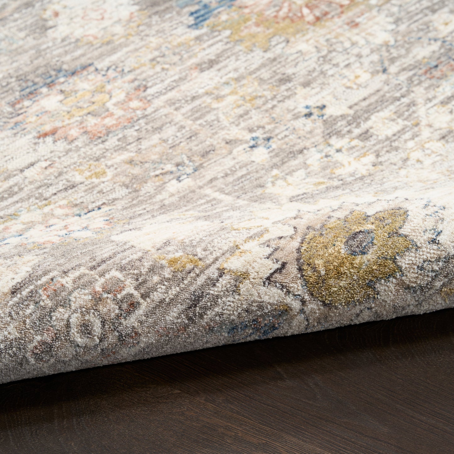 Close-up of a textured area rug with floral patterns on a wooden floor.