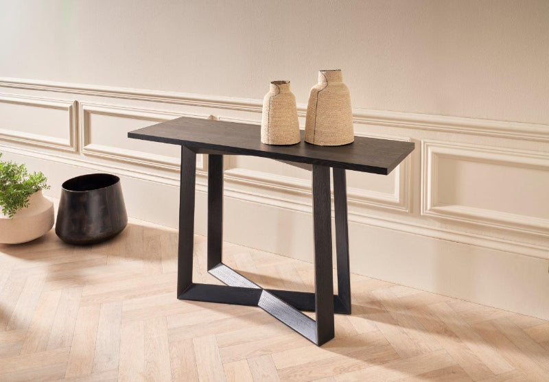 Modern black console table with decorative vases against a neutral wall.