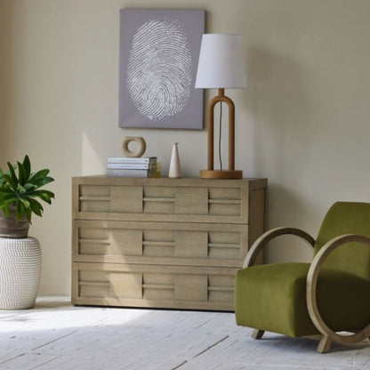 Beige dresser with decorative items in a room with a green chair and plant.