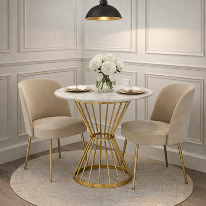 Small dining table with gold base and marble top, accompanied by two beige chairs in a room with light-colored walls.