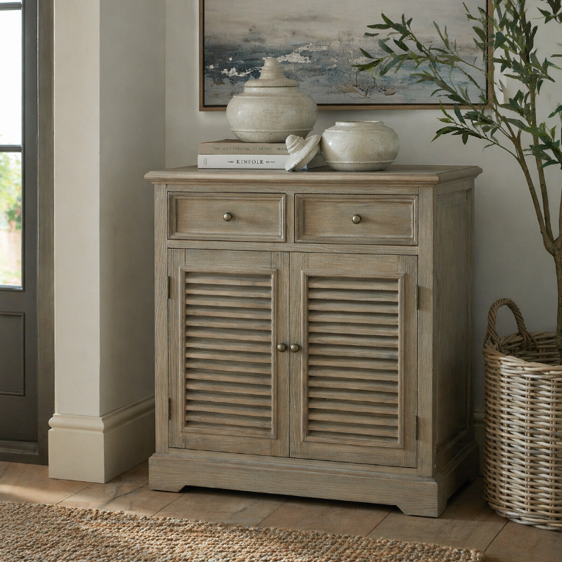 Wooden cabinet with louvered doors in a room with a plant and framed picture.