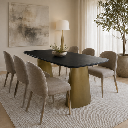 A modern dining room scene featuring a rectangular black tabletop with a large brushed brass pedestal base, surrounded by six upholstered dining chairs in a warm beige fabric. The set is styled on a textured light beige rug with a floor lamp, a large abstract painting, and a potted tree in the background.
