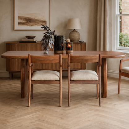 A mid-century modern wooden dining table with two matching upholstered chairs in a warm, neutral-toned dining room.
