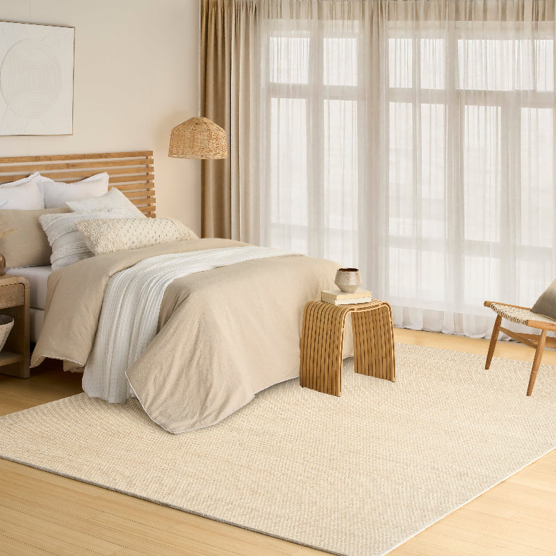 Neatly made bed in a bedroom with beige bedding, wooden headboard, and side table.
