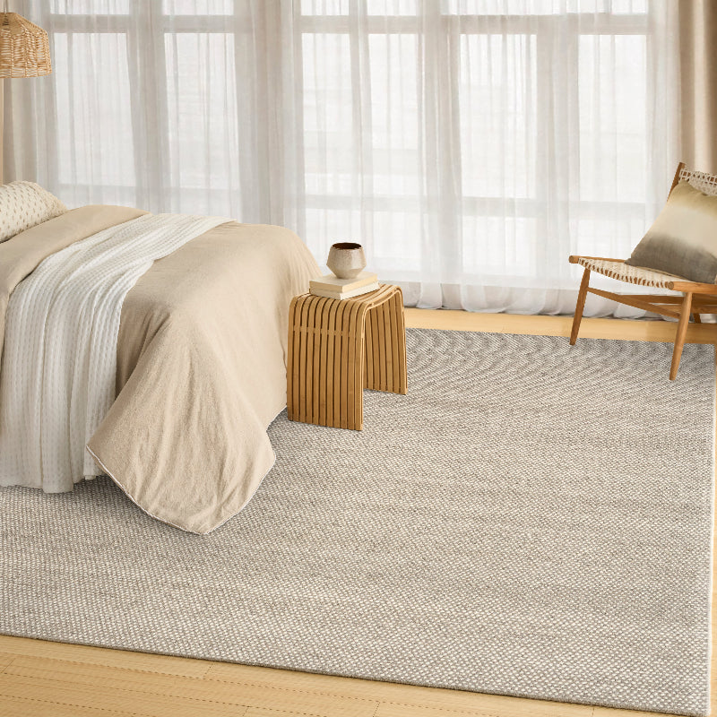 Neatly made bed with beige bedding in a room with light grey ivory rug and white curtains.
