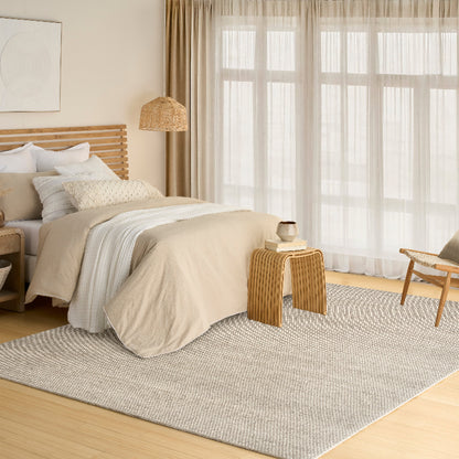 Neatly made bed in a bedroom with a lamp, chair, and large window.