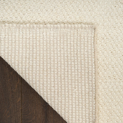 Close-up of a textured beige rug corner on a wooden floor.
