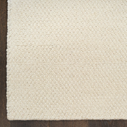 A close-up of a textured off-white or cream woven rug corner laid over a dark brown wooden floor.