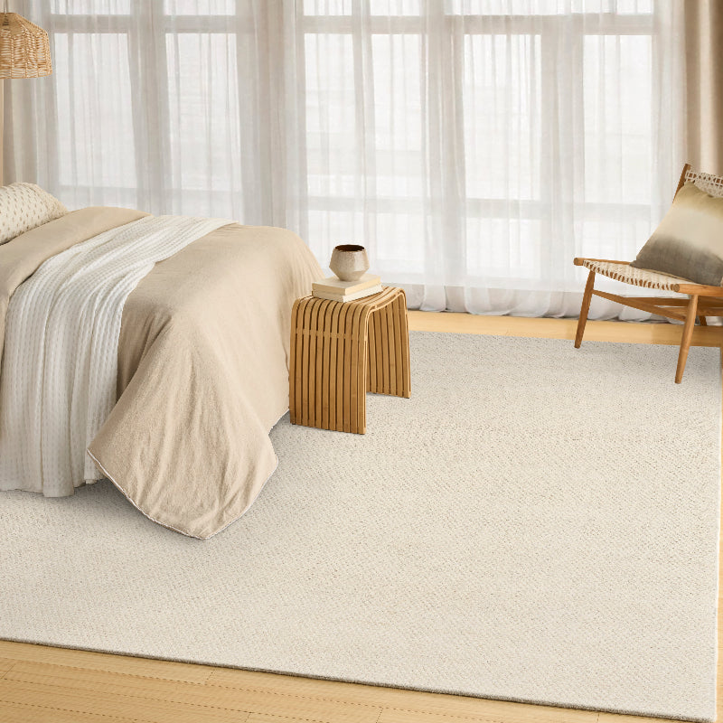 Beige bedroom with a bed, side table, and chair near large windows.