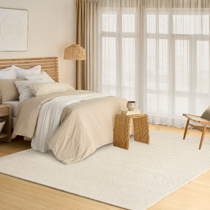 Neatly made bed in a bedroom with wooden furniture and large windows.