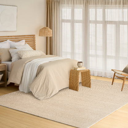 Beach-style bedroom with beige bedding, wooden furniture, and large windows.