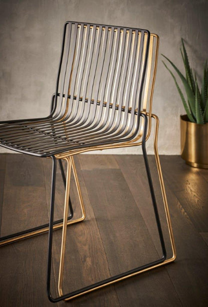 Modern chair with gold frame and black seat on a wooden floor.