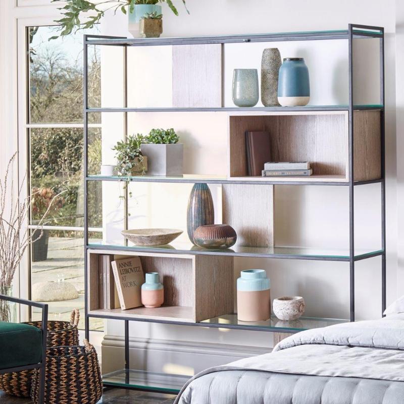 Glass shelving unit with decorative items in a room with a view of trees.