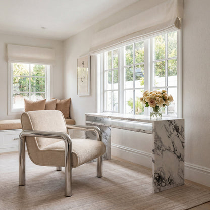 Modern interior with a beige armchair, marble desk, and large windows.