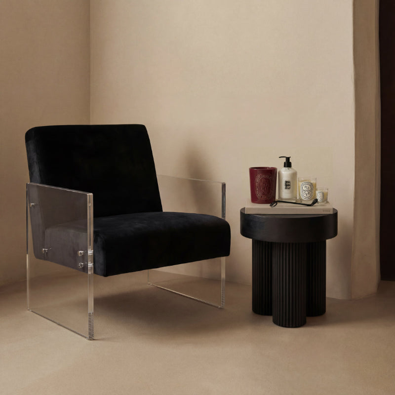 Black armchair with clear acrylic legs next to a black side table with decorative items on a beige background
