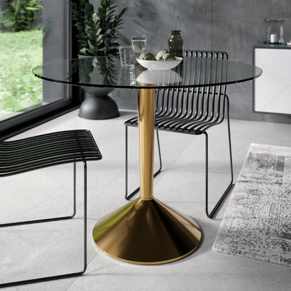 Modern dining table with gold pedestal base and black chairs in a room with large windows.