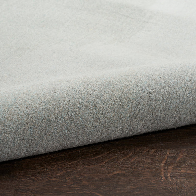 A close-up of a light gray plush or bouclé fabric, folded over to show its soft texture, resting on a dark brown wood surface.