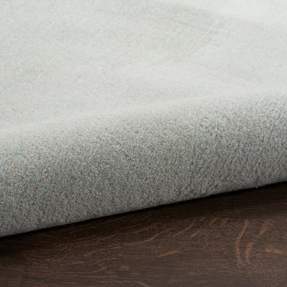 A close-up of a light gray plush or bouclé fabric, folded over to show its soft texture, resting on a dark brown wood surface.