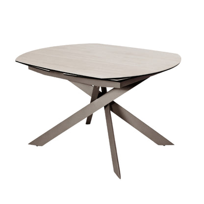 A modern oval dining table with a light beige wood-grain top and a dark gray crossed metal pedestal base, shown on a plain white background.
