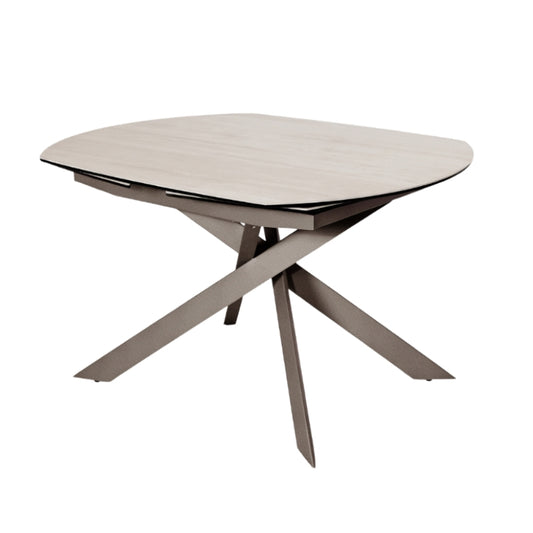 A modern oval dining table with a light beige wood-grain top and a dark gray crossed metal pedestal base, shown on a plain white background.