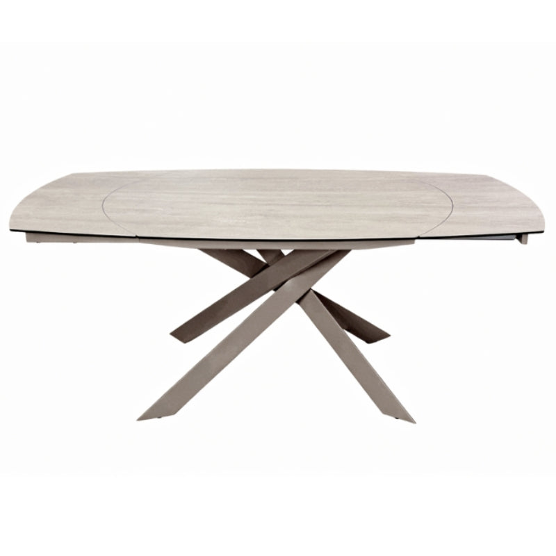 A modern oval dining table with a light beige wood-grain top and a unique X-shaped base in a taupe-brown finish, shown on a plain white background.