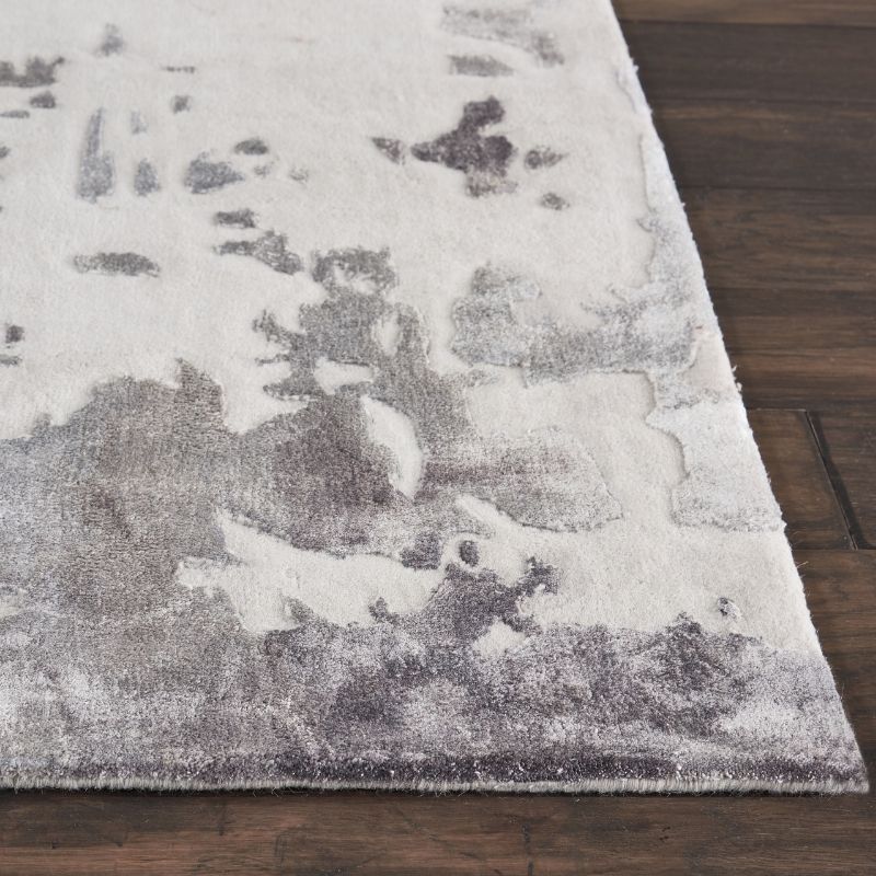 A close-up of a rectangular area rug with a distressed abstract pattern in off-white and gray, shown on a dark brown wood floor.