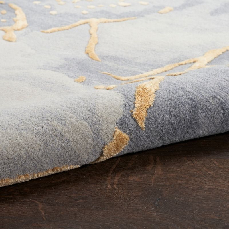 Close-up of a textured gray rug with gold leaf patterns on a wooden floor.