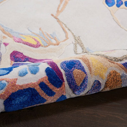 A close-up of a textured area rug with an abstract, organic pattern in vibrant blue, purple, yellow, and orange on a cream background, shown folded over to reveal its pile and underside.