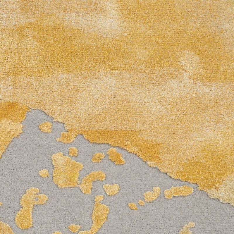 A close-up of a textured area rug featuring an abstract design with a large mustard yellow upper section and a gray lower section with irregular yellow patches.
