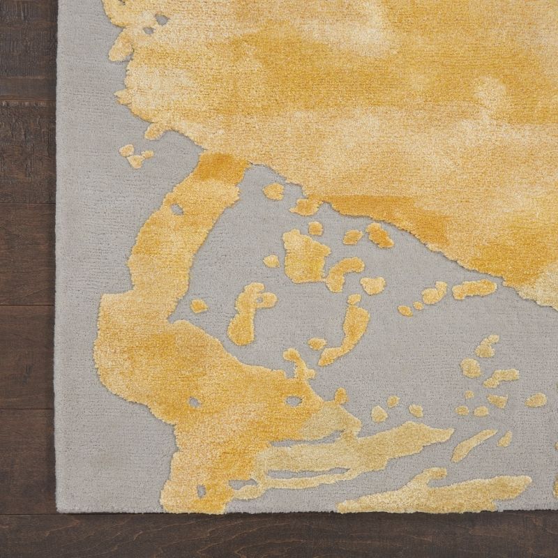 Close-up of a textured area rug corner with a mustard yellow abstract organic pattern on a light gray base, shown on a dark wood floor.