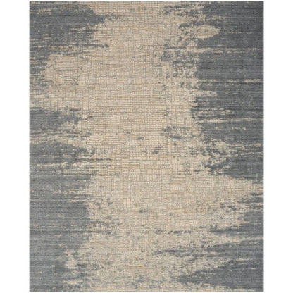 An abstract area rug with a distressed, textured pattern in slate gray and warm beige, shown flat against a white background.