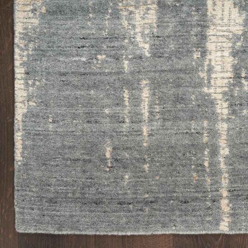 A close-up of a textured area rug with a distressed abstract pattern in gray and cream, shown on a dark wood floor.