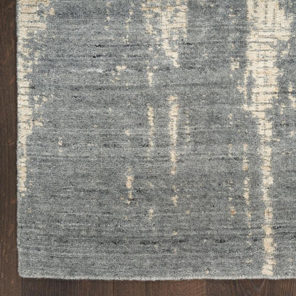 A close-up of a textured area rug with a distressed abstract pattern in gray and cream, shown on a dark wood floor.